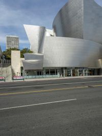 an empty street in front of a large white building with glass walls on the sides