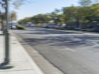 two people on bicycles riding down an empty street with trees in the background and one person on a motorcycle