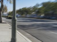 two people on bicycles riding down an empty street with trees in the background and one person on a motorcycle