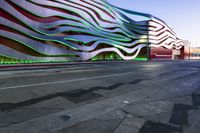 a building has metallic and green waves painted on it's side of the street