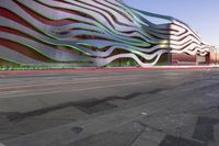 a building has metallic and green waves painted on it's side of the street