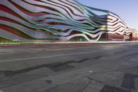 a building has metallic and green waves painted on it's side of the street