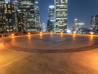 a circular paved area that looks out into the city at night with city buildings in the background