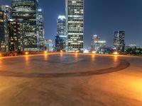 a circular paved area that looks out into the city at night with city buildings in the background