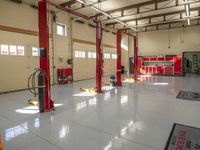 two red lifts are used to work in a garage area while a worker is at work