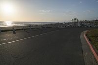 an empty road near a beach and waves as well as cars on the sand and houses on the beach