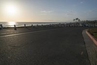 an empty road near a beach and waves as well as cars on the sand and houses on the beach