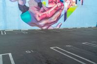 large painting on the side of a building near parking lot next to the road for pedestrians