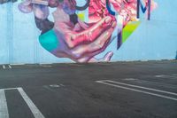 large painting on the side of a building near parking lot next to the road for pedestrians