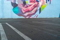 large painting on the side of a building near parking lot next to the road for pedestrians