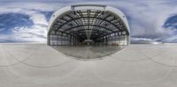 a large hangar sitting under a cloudy blue sky over ground with cars driving through it