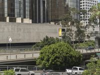 multiple cars on a road near a bridge over a freeway with tall buildings in the background