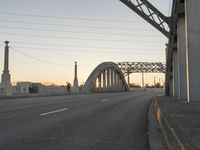 a long gray bridge and two people on it at sunset next to the freeway on which they are standing