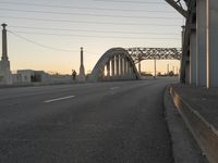 a long gray bridge and two people on it at sunset next to the freeway on which they are standing