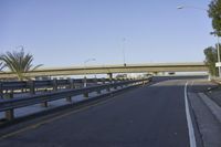 a skateboarder sitting on the side of an empty street with road and elevated overpass