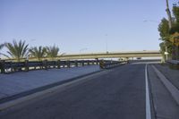 a skateboarder sitting on the side of an empty street with road and elevated overpass