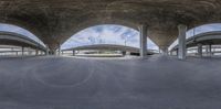 two large cement ramps under a highway overpass with two arches above them and a cloudy sky