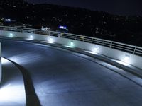 an asphalted ramp over the highway with lights at night time, illuminating cars on the side