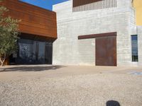 a brown building with brown walls and two metal doors on a sidewalk in front of it