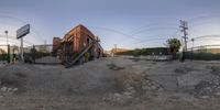 an abandoned building sitting in the dirt of an industrial setting with electric wires and barbed wire