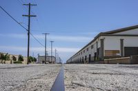 an empty parking lot on the side of an industrial building where there is no street lined with cement, poles with power lines and telephone poles