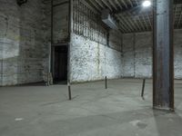 an empty room with cement walls, exposed pipes and a small window in it with lights coming