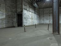 an empty room with cement walls, exposed pipes and a small window in it with lights coming