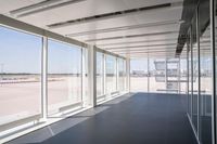 an empty room overlooking a tarmac, parked vehicles and glass walls with views of planes