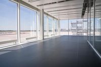 an empty room overlooking a tarmac, parked vehicles and glass walls with views of planes