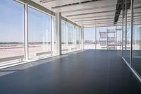 an empty room overlooking a tarmac, parked vehicles and glass walls with views of planes