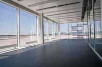 an empty room overlooking a tarmac, parked vehicles and glass walls with views of planes