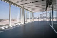 an empty room overlooking a tarmac, parked vehicles and glass walls with views of planes