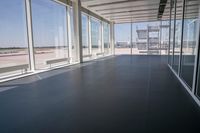 an empty room overlooking a tarmac, parked vehicles and glass walls with views of planes