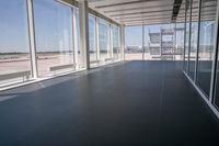 an empty room overlooking a tarmac, parked vehicles and glass walls with views of planes