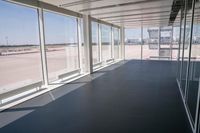 an empty room overlooking a tarmac, parked vehicles and glass walls with views of planes