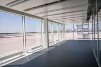 an empty room overlooking a tarmac, parked vehicles and glass walls with views of planes