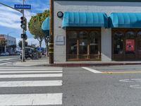 an intersection with cross walk and blue awnings on the side of the building