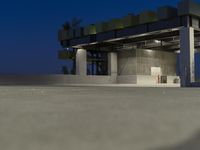 a small white kitchen outside with lights at night time, concrete area and concrete column