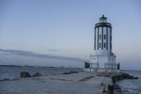 a white lighthouse is standing at the end of the pier overlooking the ocean and the city