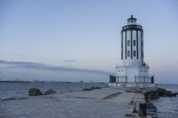 a white lighthouse is standing at the end of the pier overlooking the ocean and the city