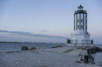 a white lighthouse is standing at the end of the pier overlooking the ocean and the city