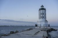 a white lighthouse is standing at the end of the pier overlooking the ocean and the city