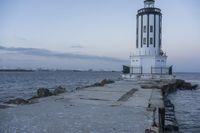 a white lighthouse is standing at the end of the pier overlooking the ocean and the city