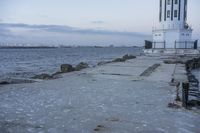 a white lighthouse is standing at the end of the pier overlooking the ocean and the city