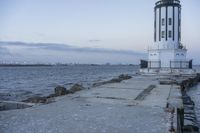 a white lighthouse is standing at the end of the pier overlooking the ocean and the city