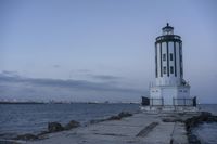 a white lighthouse is standing at the end of the pier overlooking the ocean and the city