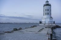 a white lighthouse is standing at the end of the pier overlooking the ocean and the city