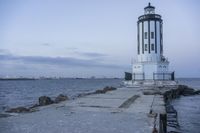 a white lighthouse is standing at the end of the pier overlooking the ocean and the city