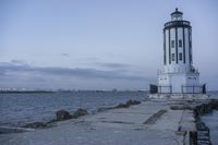 a white lighthouse is standing at the end of the pier overlooking the ocean and the city