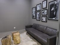 black and white pictures hang above leather couch next to petrified tree stumps, with side tables on floor